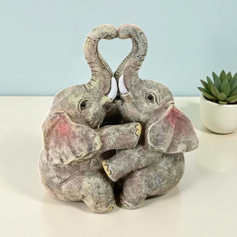 Cute resin elephant couple figurine with heart-shaped trunks, styled with modern home decor.
