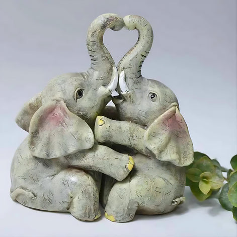 Romantic resin elephant couple figurine with heart-shaped trunks displayed next to green leaves.
