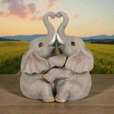Romantic elephant couple figurine with trunks forming a heart, placed in front of a sunset landscape.
