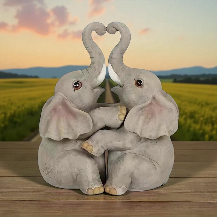 Romantic elephant couple figurine with trunks forming a heart, placed in front of a sunset landscape.
