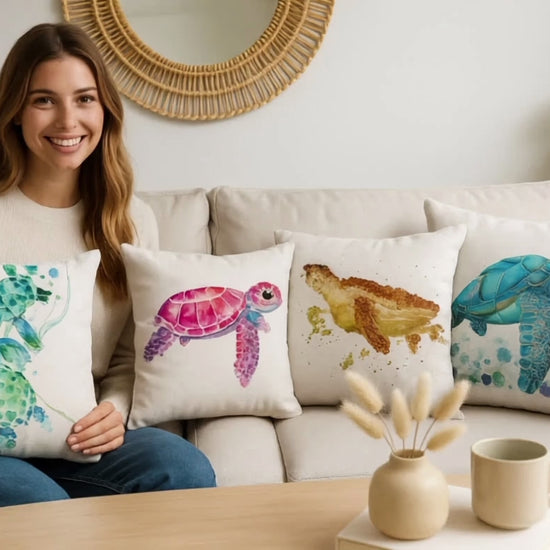 Woman sitting on sofa holding ocean turtle cushion covers – decorative pillow cases with green, pink, golden, and blue turtle designs, coastal home décor.