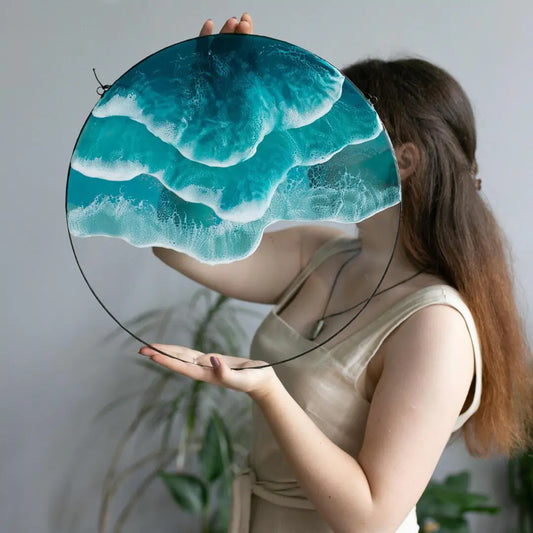 Woman holding large round acrylic wall pendant with layered ocean wave design – coastal home décor accent.
